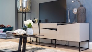 A modern living room with a flat-screen TV, a decorative vase with flowers, and a tall floor lamp. - Elegant 3BD Apartment in Earls Court (London)