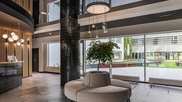 A modern lobby with a curved seating area, a large plant, and a view of the outdoor area.