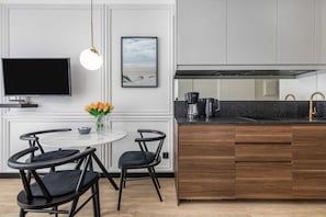 A modern kitchen with a round dining table, black chairs, a flat-screen TV, a coffee maker, and a framed picture on the wall.
