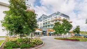 A modern building with a central entrance, outdoor seating, and a landscaped area with trees and shrubs.