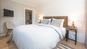 Quarto bem organizado com uma cama grande, uma cadeira, uma televisão na parede e uma mesa de cabeceira com abajur.