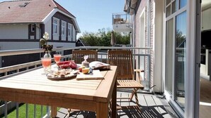 A wooden table set with food and drinks on a balcony with a view of a house and greenery. - Silbermöwe im Lindenhof - designer apartment in country house style (Wangerooge)