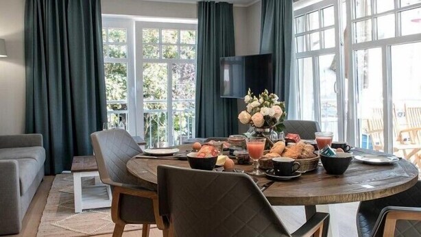 A dining area with a round table set for breakfast, featuring bread, pastries, and beverages. - Silbermöwe im Lindenhof - designer apartment in country house style (Wangerooge)