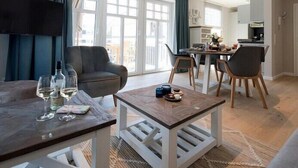 A modern living room with a sofa, a coffee table, and a dining area with chairs and a table. - Silbermöwe im Lindenhof - designer apartment in country house style (Wangerooge)