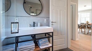 A modern bathroom with a white sink, a round mirror, and a towel rack. - Silbermöwe im Lindenhof - designer apartment in country house style (Wangerooge)