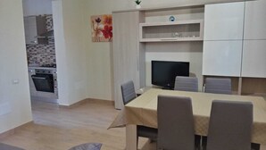 A modern kitchen with white cabinets, a dining area with a table and chairs, and a TV. - Bright Apartment with Terrace Cin Code IT092080C2000Q2483 (Sinnai)
