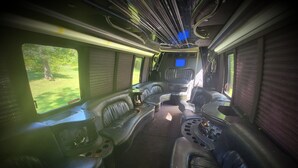 A train interior with leather seating, a control panel, and windows offering a view of greenery. - Limo Party Tailgate Bus (State College)