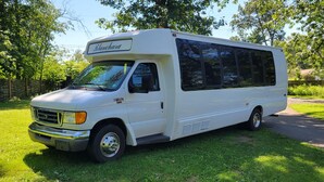 A white RV with a 'Blanchard' sign on the front, parked on grass with trees in the background. - Limo Party Tailgate Bus (State College)