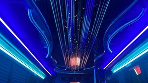 A luxurious interior with leather seating, a bar area, and a ceiling with vertical light fixtures. - Limo Party Tailgate Bus (State College)