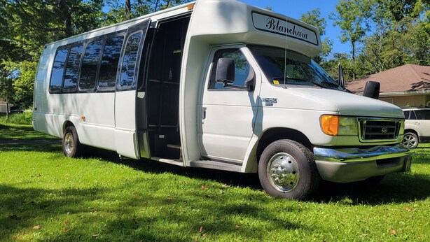 A white RV with a sliding door, parked on grass. - Limo Party Tailgate Bus (State College)