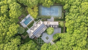 Vue aérienne d’une propriété dotée d’une piscine, d’un court de tennis et d’un bâtiment dont le toit est en pente.