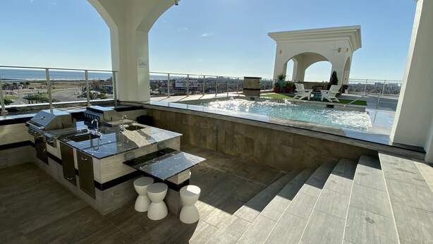 Zona de piscina en la azotea con bar y asientos, con vistas a un paisaje urbano.