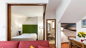 Una stanza con un divano rosso, un tavolo da pranzo con sedie, un letto con testiera verde e un bagno con lavandino e specchio.