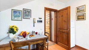 Un'area pranzo con un tavolo di legno, sedie, una tovaglia a quadri e un vaso di fiori gialli. Alle pareti ci sono quadri incorniciati e sullo sfondo una porta in legno.