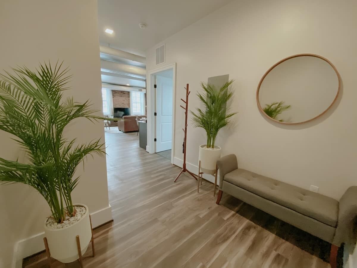 A hallway with a wooden floor, a beige sofa, and two potted plants.