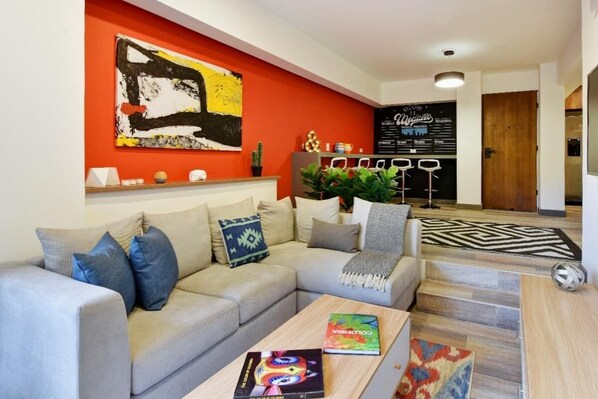 A modern living room with a grey sofa, a coffee table with books, a vibrant red accent wall, and a black and white rug. - Homey Atmosphere 3BR Flat steps from Provenza with A/C (Medellín)