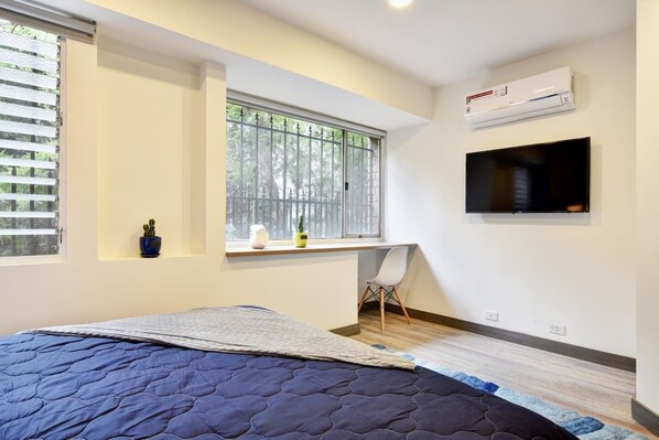 Quarto com cama, escrivaninha, cadeira, televisão e ar condicionado.