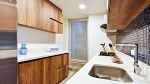 Eine moderne Küche mit Holzschränken, einer weißen Arbeitsplatte, einem Edelstahl-Spülbecken und einer gefliesten Spritzschutzwand.