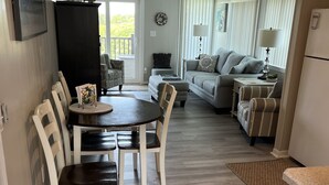 A dining area with a table and chairs, a sofa, and a small side table with a lamp. - Atlantic Beach Condo within walking distance to the beach (Atlantic Beach)