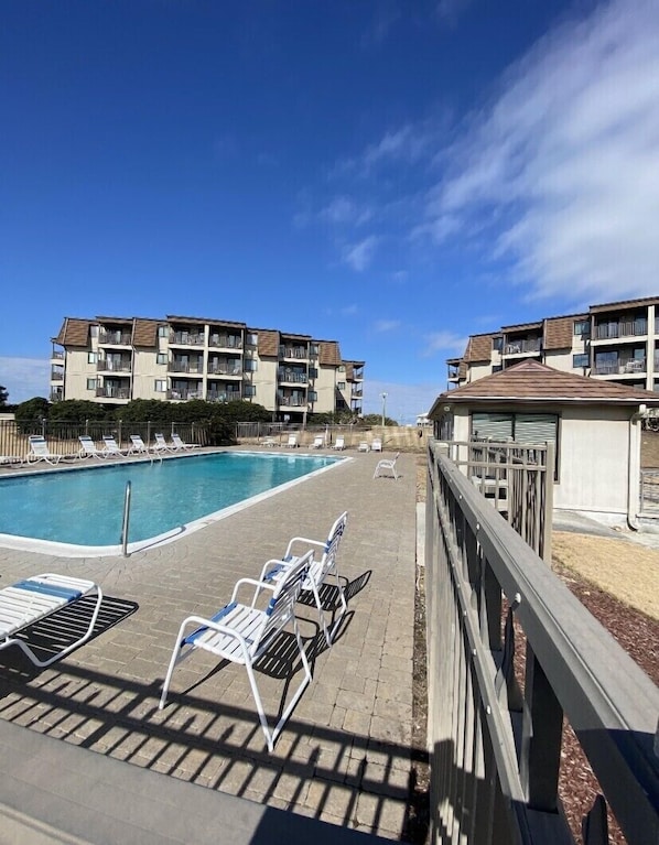 A poolside area with lounge chairs and a clear view of a building with balconies.