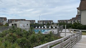 A wooden boardwalk leading to a swimming pool area with a view of residential buildings in the background. - Atlantic Beach Condo within walking distance to the beach (Atlantic Beach)