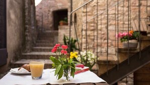 A table with a glass of orange juice, a croissant, and a small potted plant with red flowers. - Emerald apartment with valley view in the historic center (Spello)