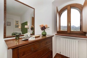 A wooden dresser with a mirror, a vase with flowers, and a window with a view of the countryside.