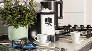 A kitchen counter with a coffee maker, two cups, a packet of coffee, and a potted plant. - Emerald apartment with valley view in the historic center (Spello)