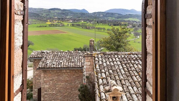 A view through an arched window overlooking a green field and distant hills. - Emerald apartment with valley view in the historic center (Spello)