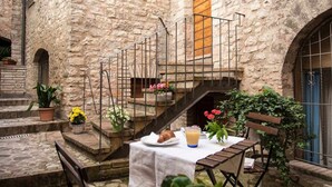 A stone courtyard with a table set for two, a staircase, and potted plants. - Emerald apartment with valley view in the historic center (Spello)