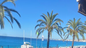 A balcony with a view of the beach, palm trees, and a clear blue sky. - Villa Avec Piscine Chauffée Nice Collines (Nice)