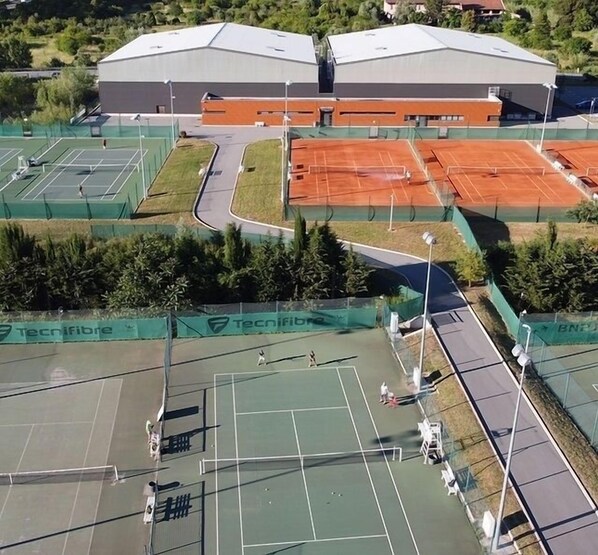 An aerial view of a sports complex with multiple tennis courts, a covered area, and a large building with a flat roof. - Villa Avec Piscine Chauffée Nice Collines (Nice)