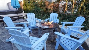 A patio area with four blue Adirondack chairs arranged around a stone fire pit with a fire burning. - Beach Gem! 2 bd with Hot Tub/3.7mi beach/.5mi outlets (Rehoboth Beach)