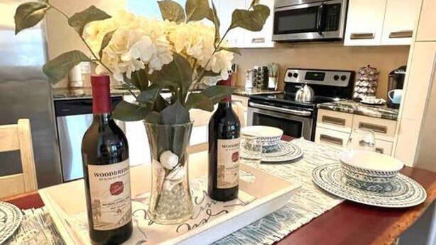 A kitchen with white cabinets, a microwave, and a stove. There is a tray with two bottles of wine and a vase with flowers on the counter. - Beach Gem! 2 bd with Hot Tub/3.7mi beach/.5mi outlets (Rehoboth Beach)