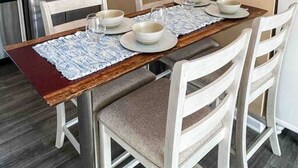 Un comedor con una mesa de madera, sillas blancas y un refrigerador de acero inoxidable.