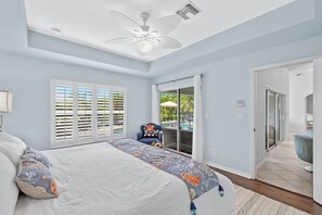 A bedroom with a large bed, a ceiling fan, and a view of a pool through a sliding glass door.