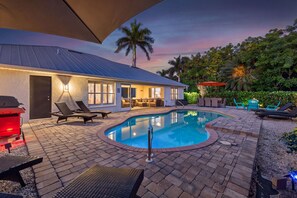 Ein Poolbereich mit Liegestühlen, einem Grill und einem Haus mit überdachter Terrasse.