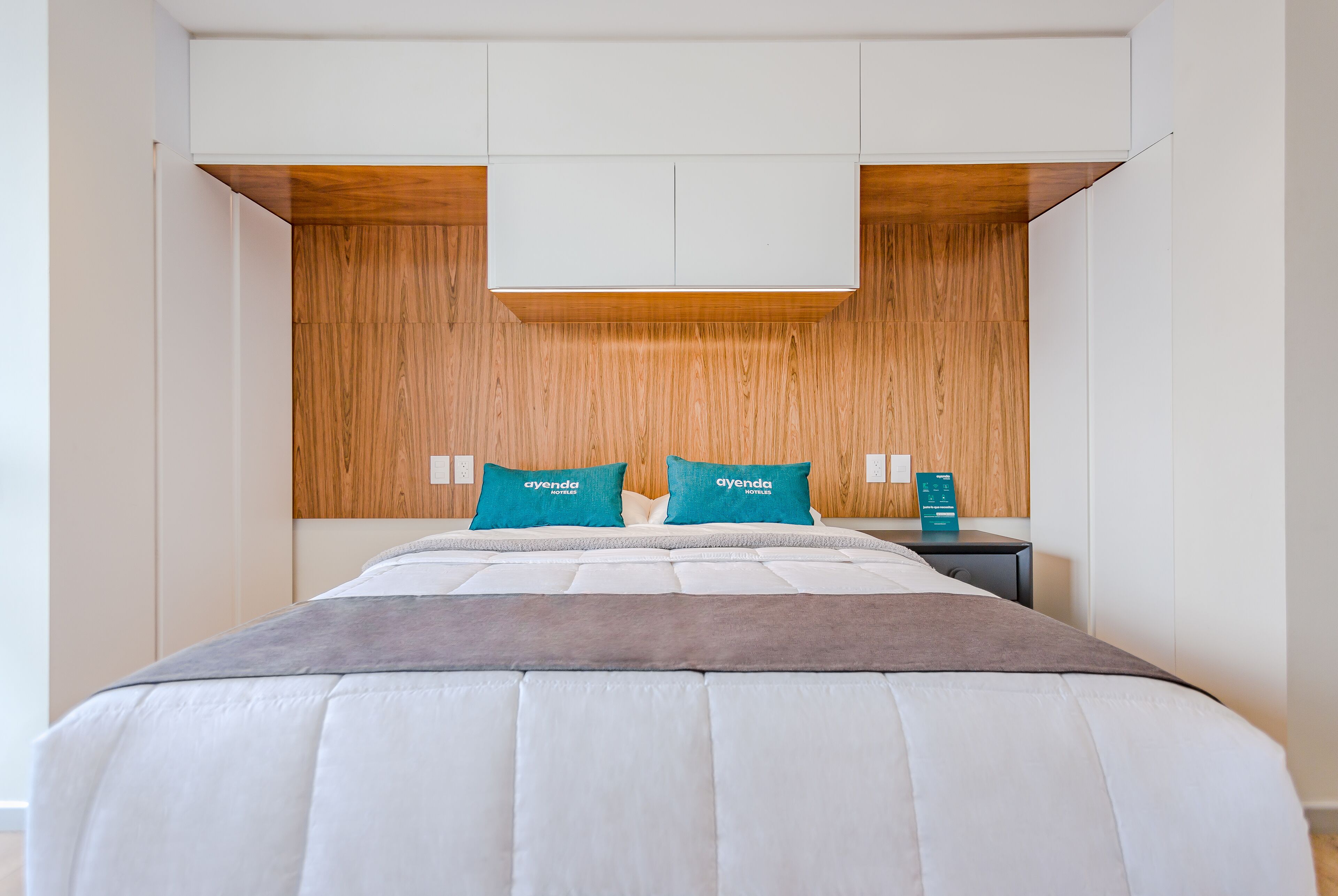 Una habitación de hotel moderna con una cama grande, dos almohadas, una mesita de noche y una pared decorativa de madera.