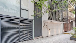A modern building with a closed shuttered entrance, a tiled ground, and a small tree in the foreground.