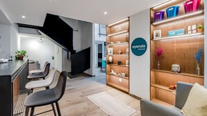 A modern hotel lobby with a bar area, wooden shelving with decor, and a staircase.