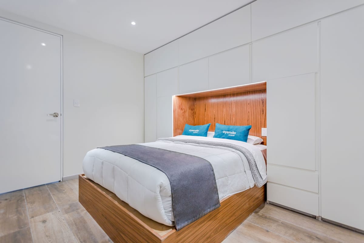 Een moderne hotelkamer met een houten hoofdeinde, een groot bed met witte beddengoed en twee blauwe kussens.