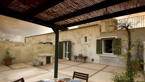 Zona de porxo coberta amb taula preparada per dinar, una planta en test i vista d'un edifici amb balcó.