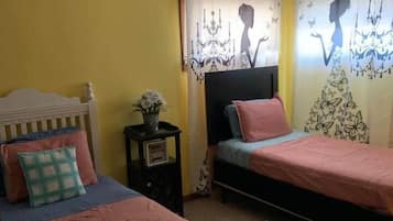 Una habitación con dos camas, una mesita de noche con una lámpara y una ventana con cortinas.