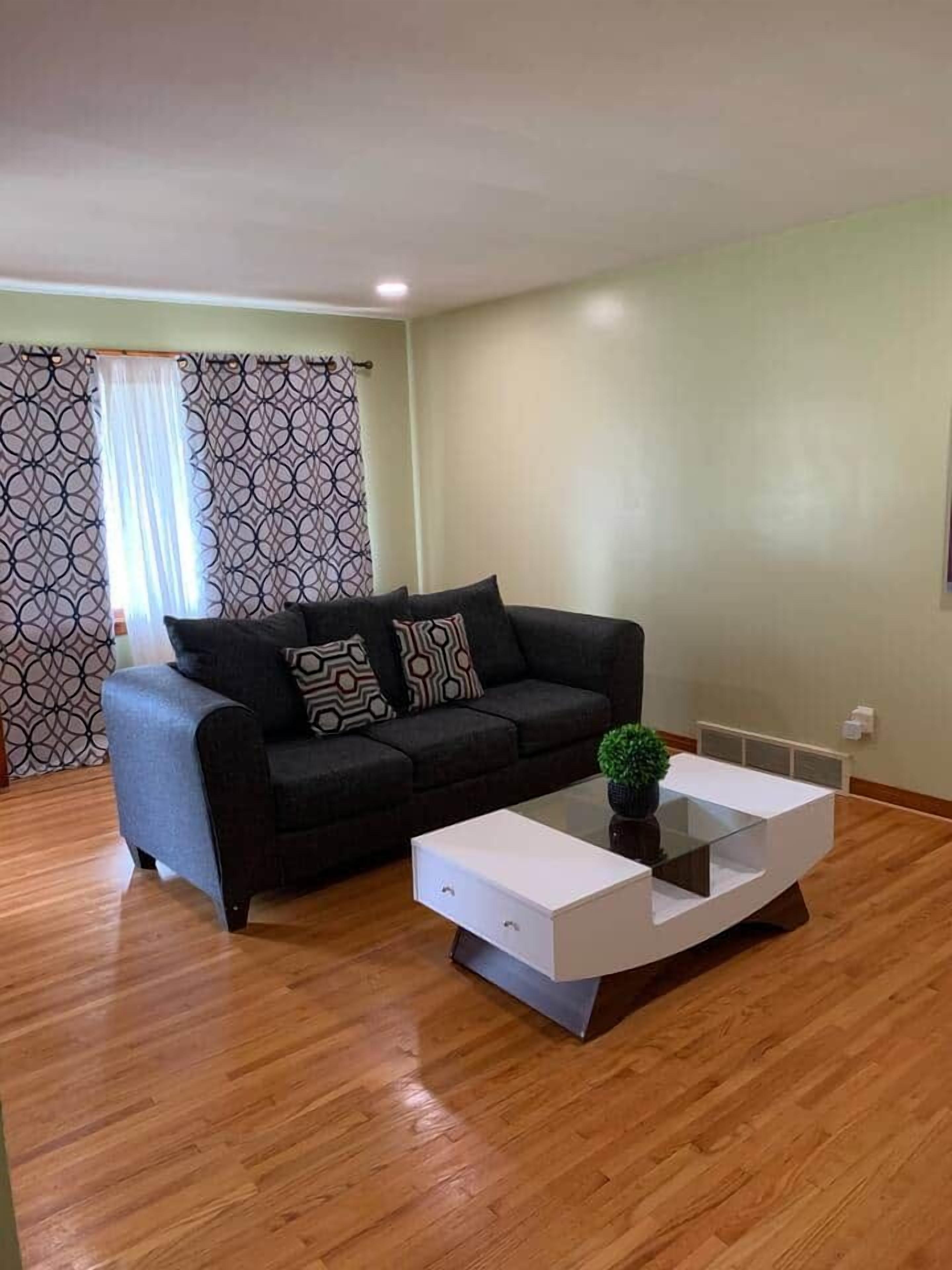 Una sala de estar con un sofá negro, cojines estampados, una mesita de centro de cristal y una pequeña planta en maceta.