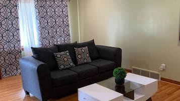 Una sala de estar con un sofá negro, cojines estampados, una mesita de centro de cristal y una pequeña planta en maceta.