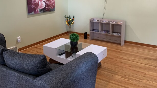 A living room with a grey sofa, a coffee table with a plant, a flat-screen TV mounted on the wall, and a bookshelf.