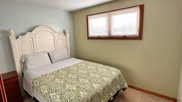 A bedroom with a single bed, a window with blinds, a ceiling vent, and a carpeted floor.
