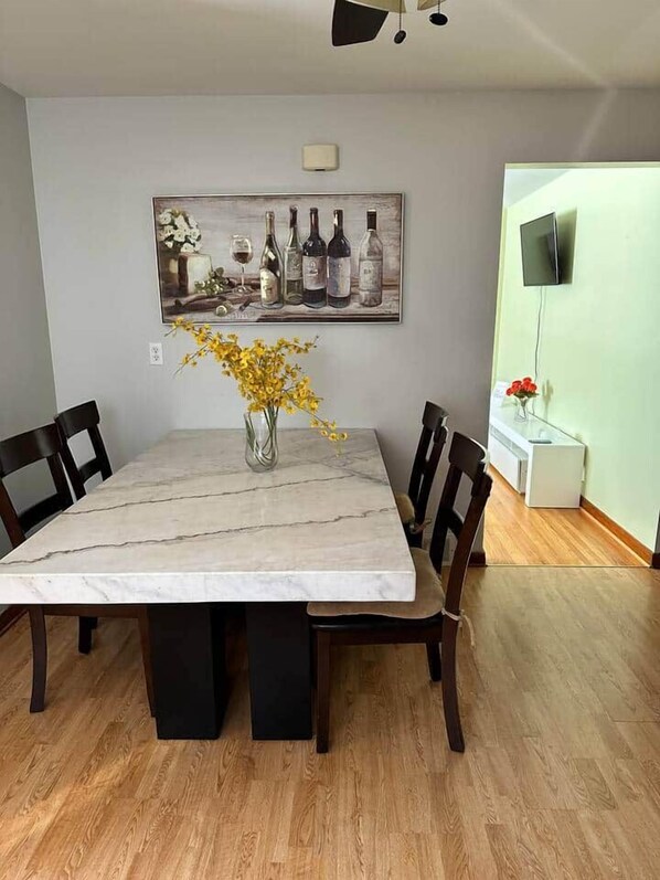 A dining area with a marble table, four chairs, a vase with yellow flowers, and a painting above the table.