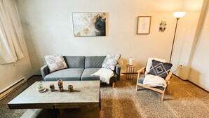 Un salon avec un canapé gris, une table basse, un fauteuil et un lampadaire.
