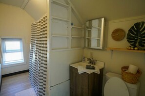 Une salle de bain avec un rideau de douche, un lavabo, des toilettes, un miroir et une fenêtre avec des stores.